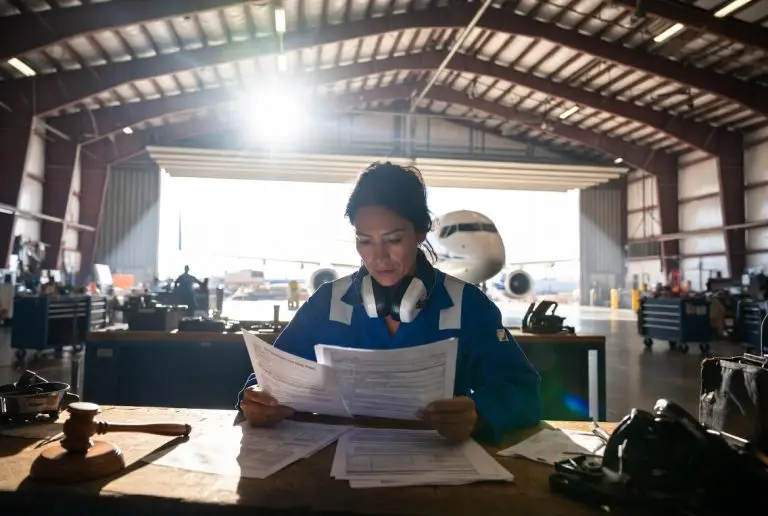alt="Female aircraft mechanic reviewing third party claim and workers compensation documents in airplane hangar after work injury in California"