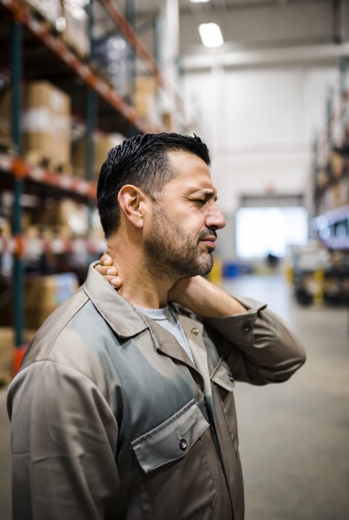 Injured warehouse worker holding his neck in pain from a work-related cervical spine injury in California — workers compensation help